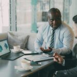 Two business professionals engaged in discussion over laptops and documents.
